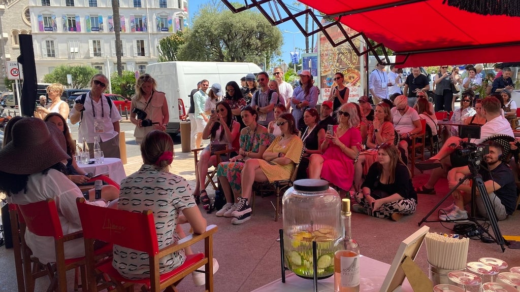 A crowd of people watches speakers in an outdoor tent setting.