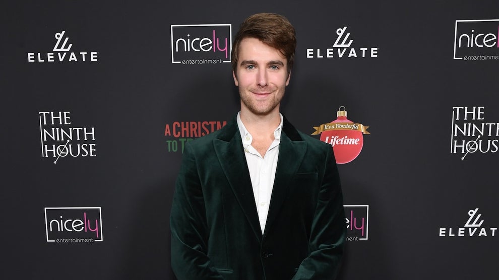 A man in a green sports coat stands in front of a step-and-repeat.