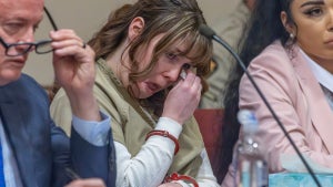 Hannah Gutierrez-Reed, a young woman wearing handcuffs and a prison uniform, wipes away tears while sitting in court with lawyers at her side.