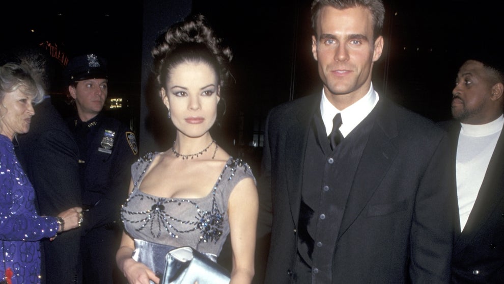 A woman walks the red carpet in a dress with a man accompanying her wearing a suit and buttoned-up vest.