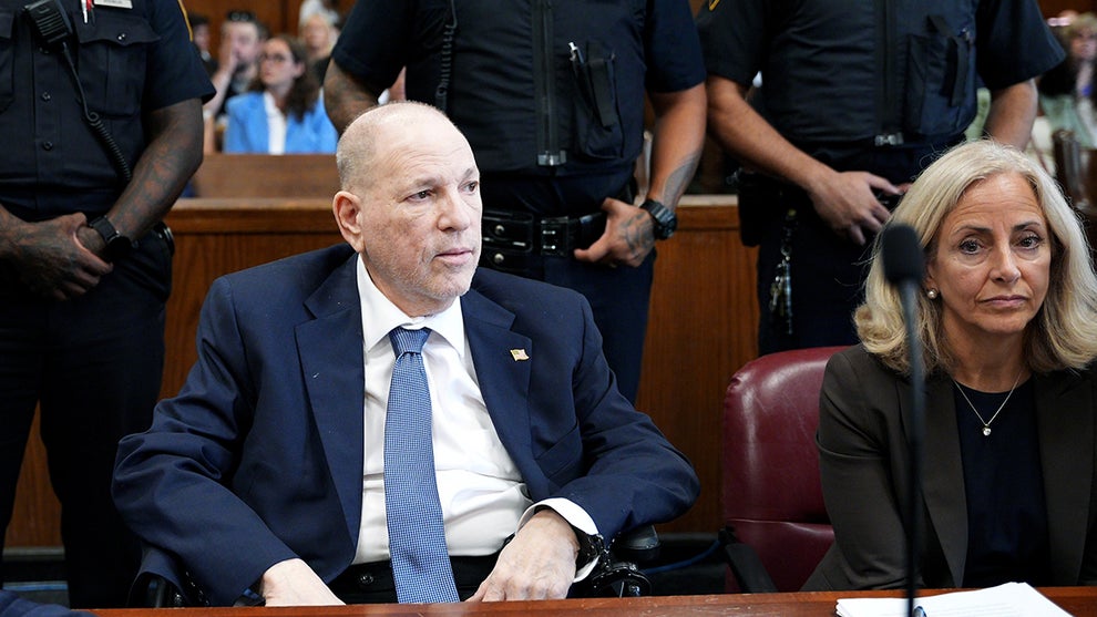 A pale-looking Harvey Weinstein, wearing a dark blue suit and tie, sits in court as prosecutors argue a date for his retrial.