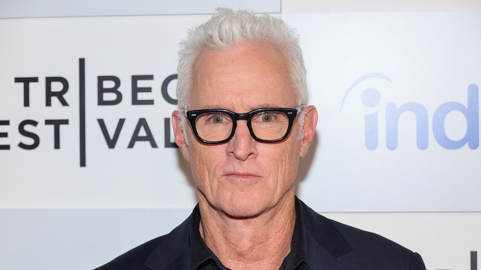 An older man wears thick black-rim glasses and has stark white hair, standing against a step-and-repeat promoting the Tribeca Film Festival.