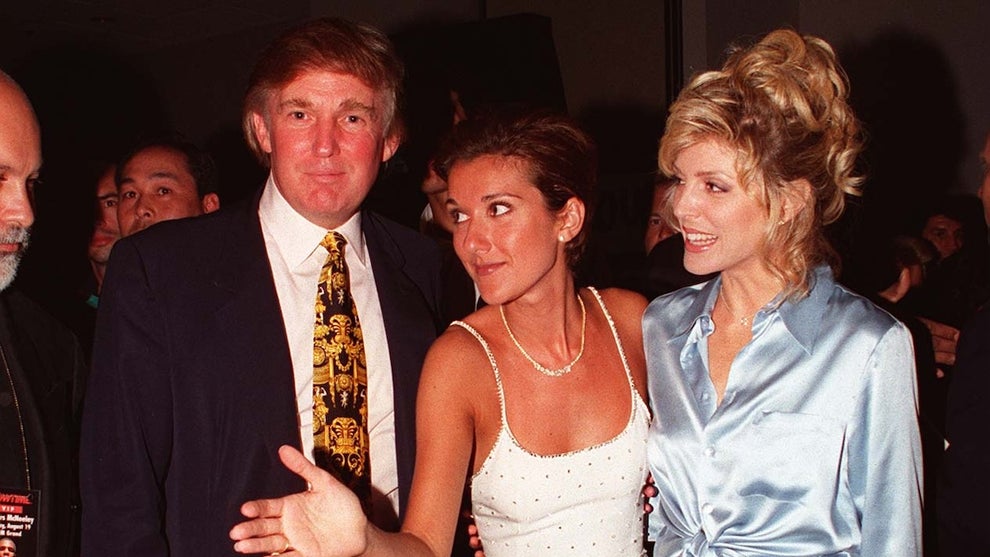 A man in a suit stands next to two women, all with light-toned skin.