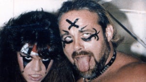 A woman and a man dressed in goth-esque dark makeup, the man wearing a chain around his neck.
