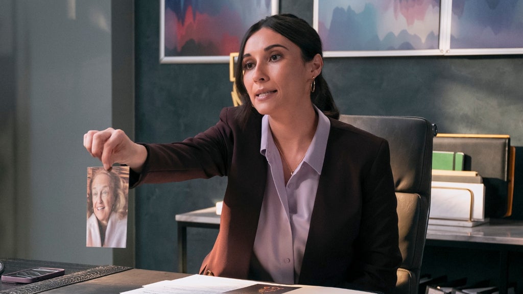 A woman in a suit holds out a photograph of an older woman across a desk