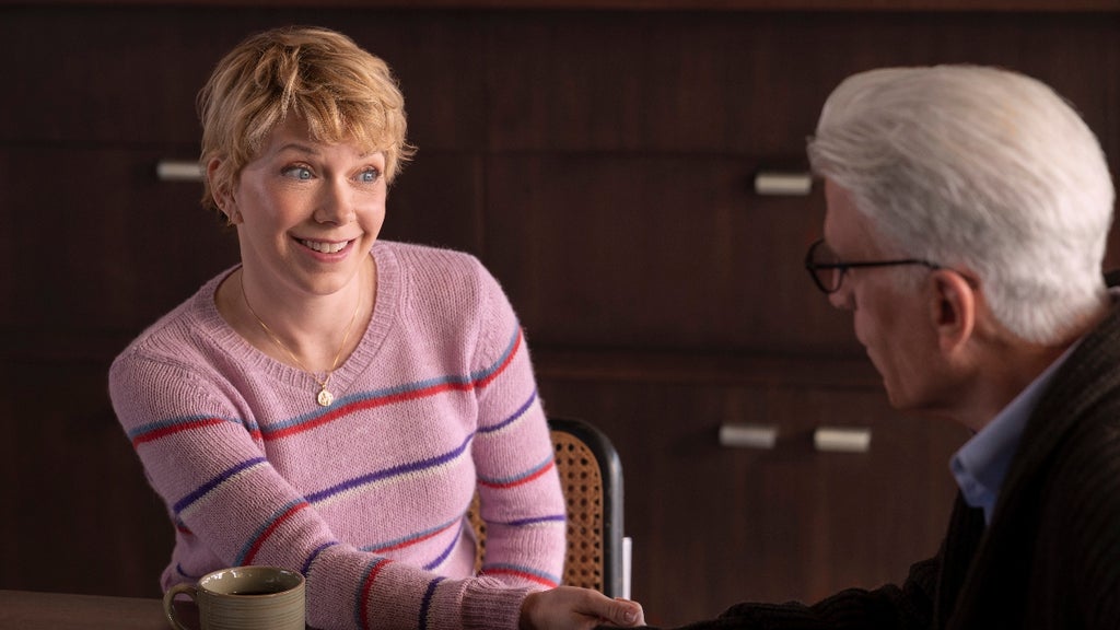 A woman in a striped pink sweater with short blonde hair smiles at her father