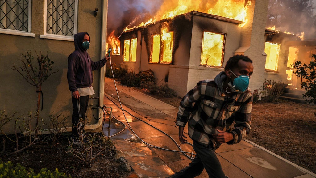 Samuel Girma runs to get another hose as he helps try to prevent a home from catching fire during the Eaton Fire. (Credit: Robert Gauthier/Getty Images)