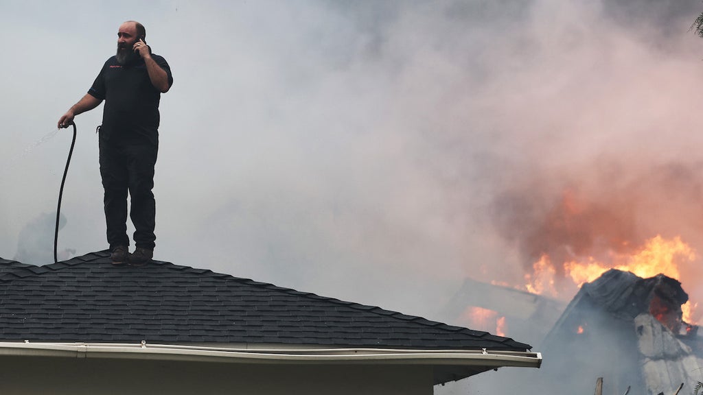 An Eaton resident stands atop a roof to spray the fire with a garden hose.