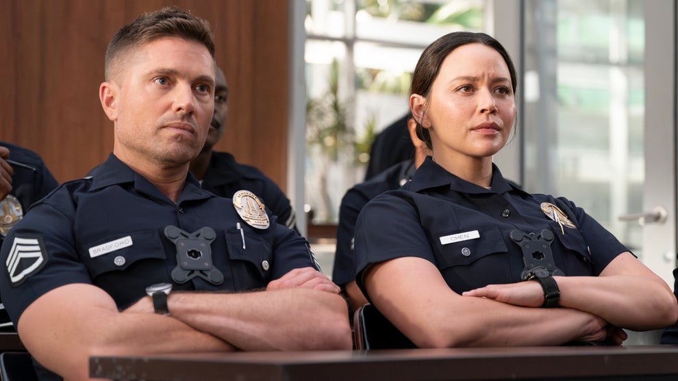 A male cop and female cop sit side by side, looking ahead and crossing their arms in a matching manner.