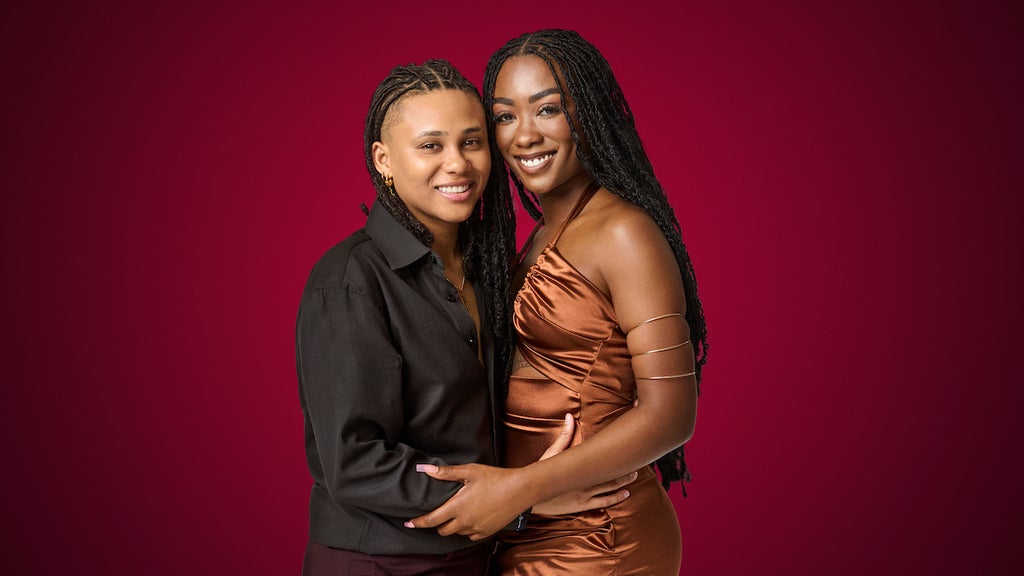 Two women smile and hug posing in front of a red background. AJ and Britney in Season 2 of "The Ultimatum: Queer Love" (Credit: Melody Timothee / Netflix)