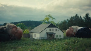 A still from Miro Remo’s “Better Go Mad in the Wild” with identical twins Ondřej and František Klišíkn laying down besides a small model version of their remote home.