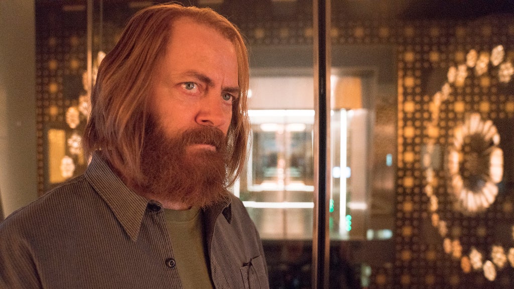 A man with a beard and long hair stares intently out of frame with a big, glowing computer screen behind him