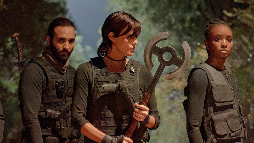 Three immortals in black tactical gear stand in formation, Charlize Theron wielding a large axe at the center