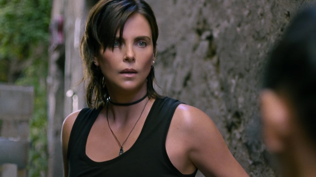 A battle-worn woman with short dark hair and a choker stands alert in an alleyway, ready for confrontation.