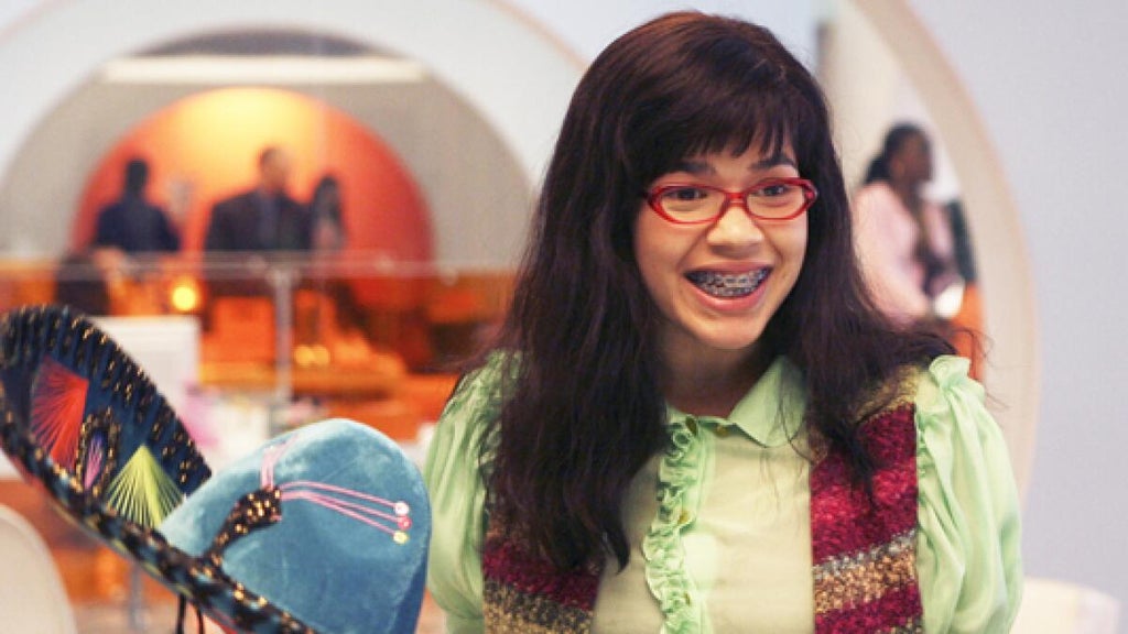 A young woman with glasses and braces smiles enthusiastically in a chic office setting