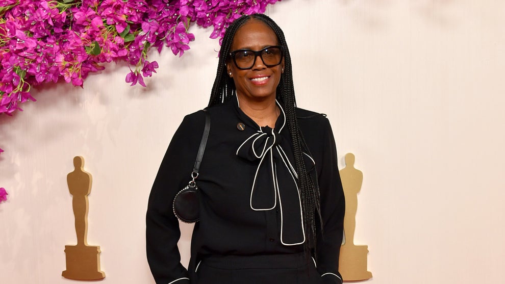 Kim Taylor-Coleman poses in front of a backdrop with pink flowers and small golden Oscars logos at the 96th Annual Academy Awards