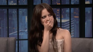 A young woman with dark hair covers her mouth with her hand in shock
