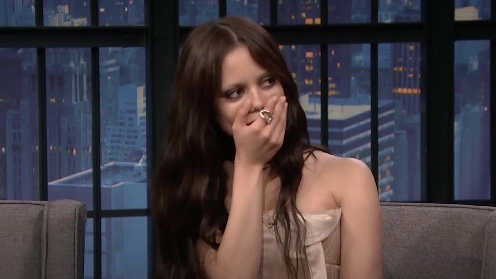 A young woman with dark hair covers her mouth with her hand in shock