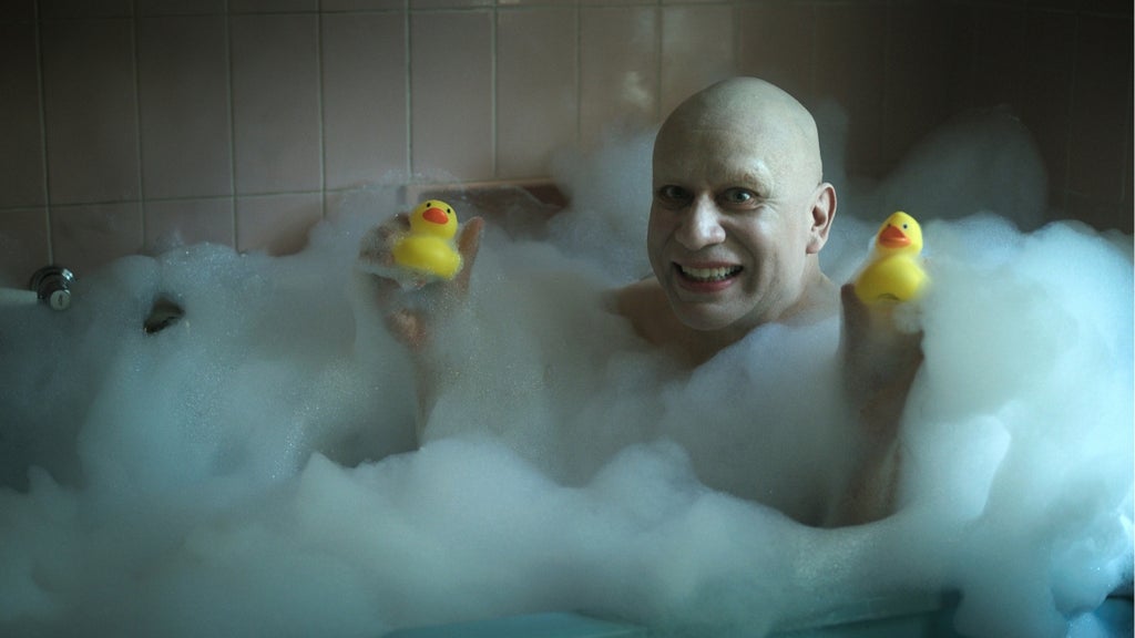 Fred Armisen plays Uncle Fester in Wednesday Season 2, smiling in a bubble bath while holding two rubber duckies