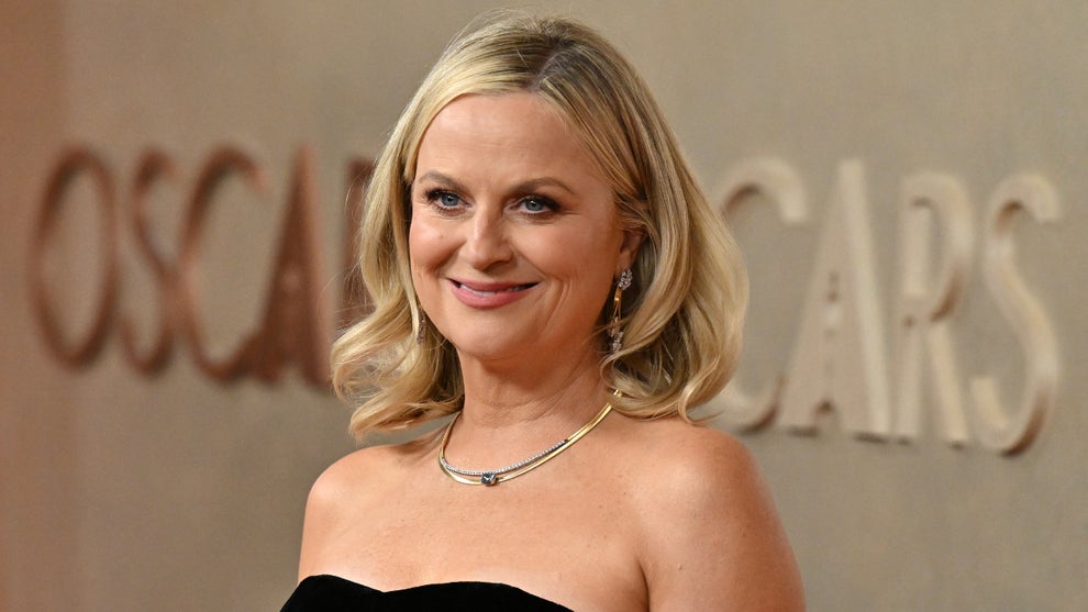 Amy Poehler stands in front of an Oscars backdrop
