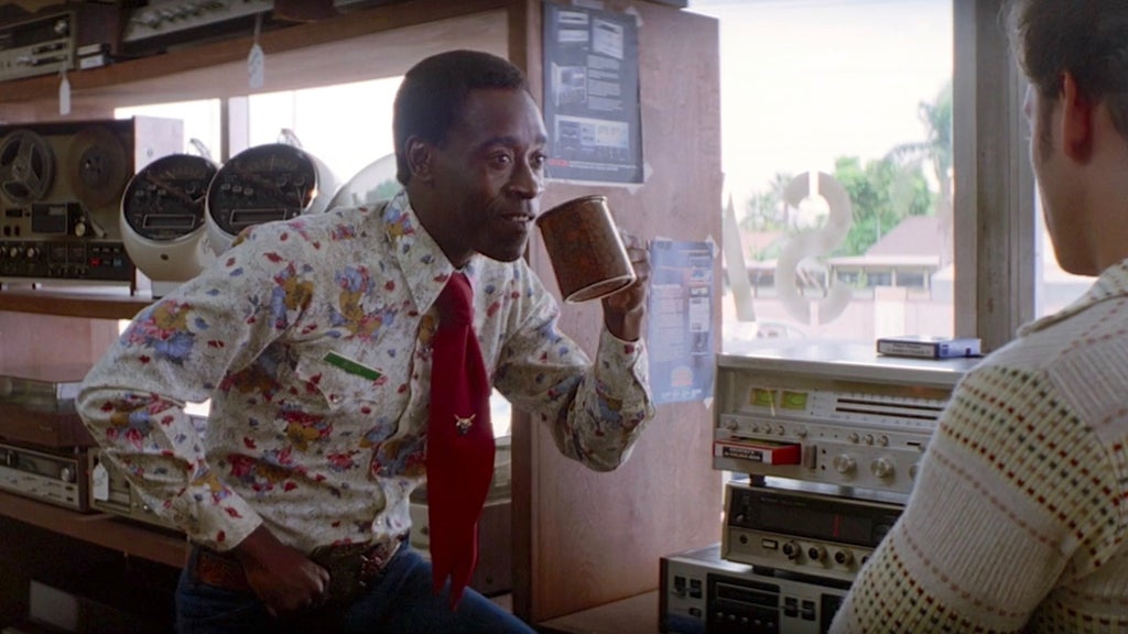 Don Cheadle holds a cup of coffee to his mouth while talking to a customer at a stereo store in "Boogie Nights"