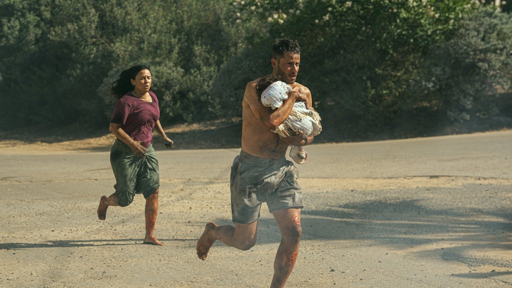 A shirtless man carrying a small child runs with a woman running behind him