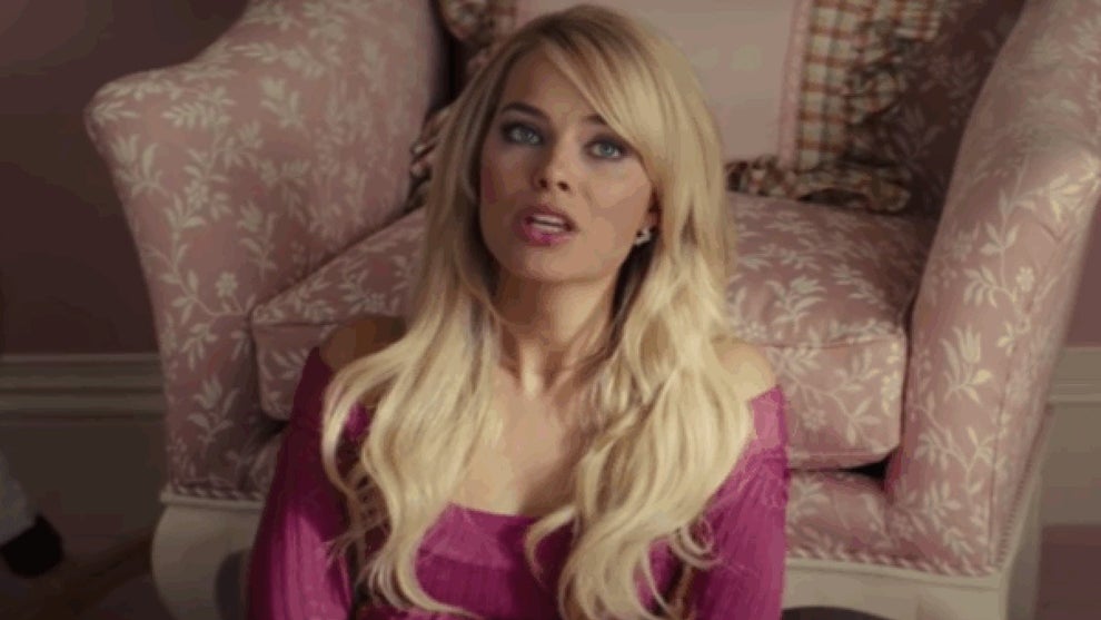 A woman with long blonde hair, wearing a pink halter top, sitting in front of an armchair