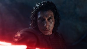 Adam Driver points a red lightsaber forward as an unmasked Kylo Ren