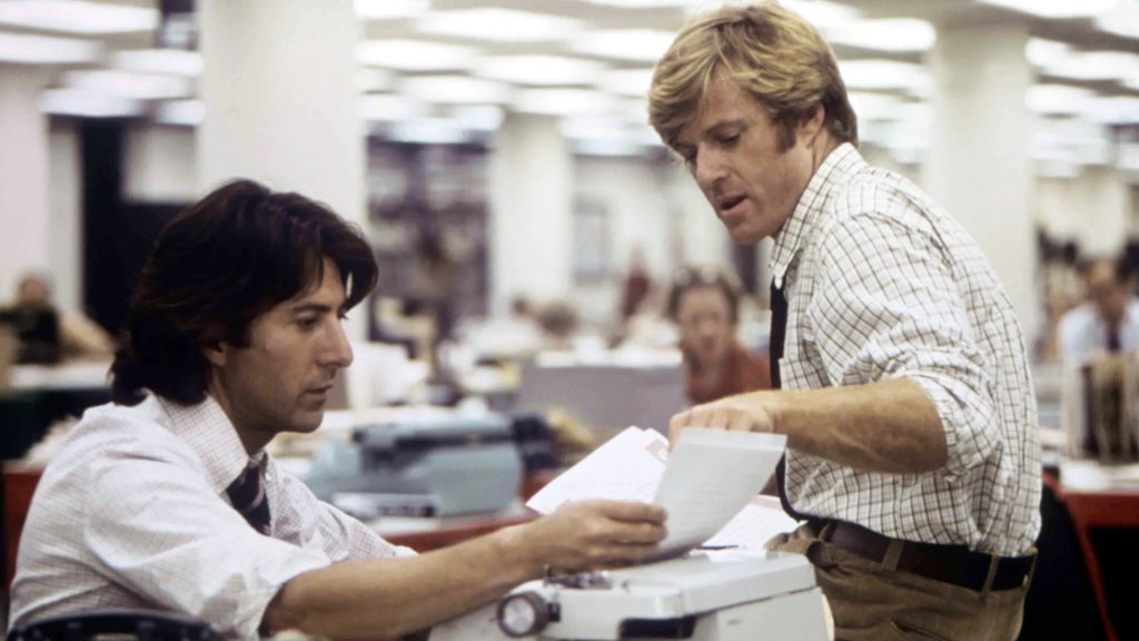 Dustin Hoffman (left) and Robert Redford (right) sit at a desk and look at papers in "All the President's Men"