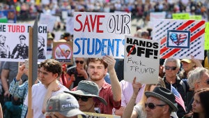 Students protest with signs such as "SAVE OUR STUDNETS" and "HANDS OFF!"