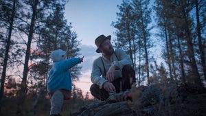 Joel Edgerton crouches next to a toddler who points at the sky in "Train Dreams"