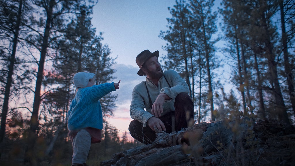Joel Edgerton crouches next to a toddler who points at the sky in "Train Dreams"