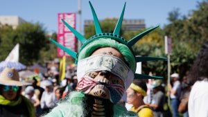 A protester dressed as the Statue of Liberty wears a blind fold and a gag as she waits for the march to begin at the "No Kings" protest on October 18, 2025 in Los Angeles, California