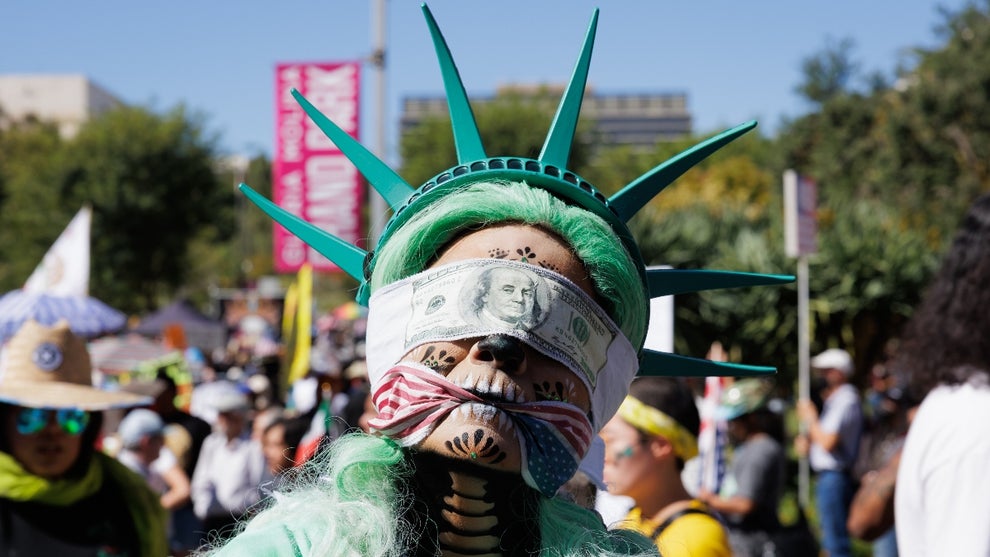 A protester dressed as the Statue of Liberty wears a blind fold and a gag as she waits for the march to begin at the "No Kings" protest on October 18, 2025 in Los Angeles, California