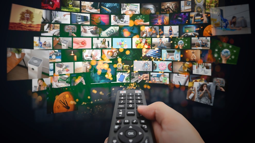 A hand holding a remote sits in the foreground center frame with a cascade of screens showing different videos in the background
