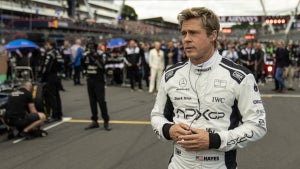 Brad Pitt walks on an F1 track in uniform wearing earbuds in "F1: The Movie"