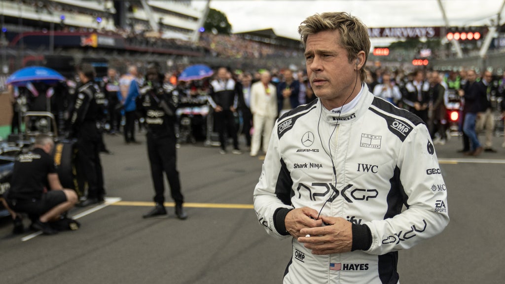 Brad Pitt walks on an F1 track in uniform wearing earbuds in "F1: The Movie"