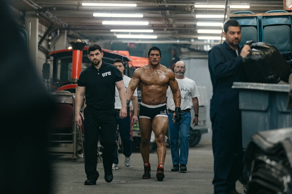 Dwayne Johnson is surrounded by a group of people in a tunnel as he walks to the ring in "The Smashing Machine
