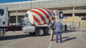 Two men stand next to a cement mixing truck