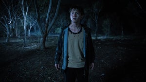 Joe Bird stands alone in a dark forest looking at something out of frame in a still from "Leviticus."