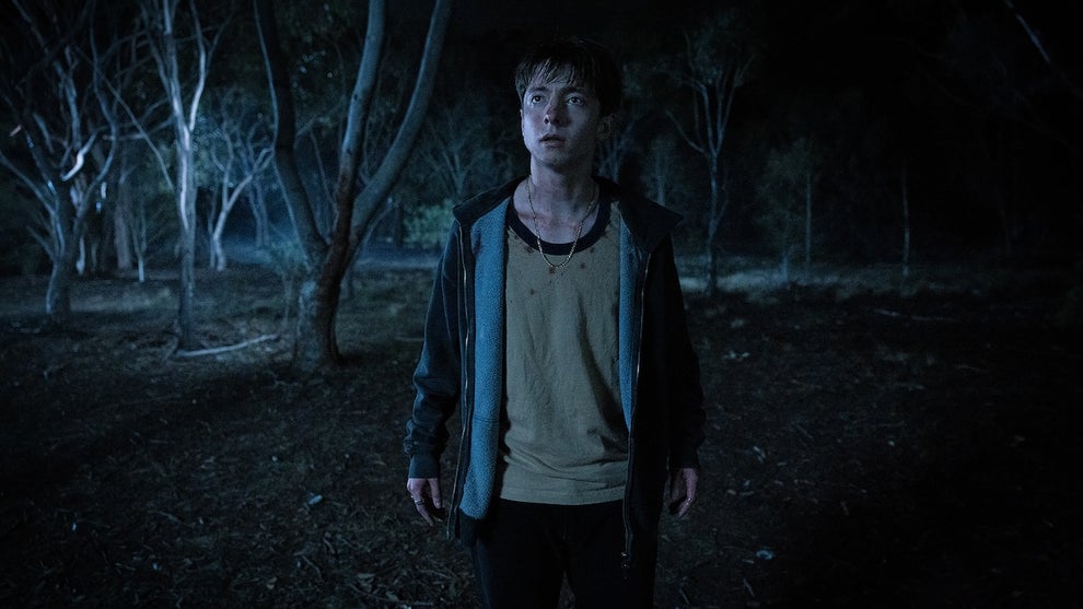 Joe Bird stands alone in a dark forest looking at something out of frame in a still from "Leviticus."
