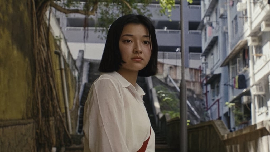 Michelle Mao standing on a large staircase in Hong Kong looking at something or someone out of frame in a still from Kogonada's Zi.