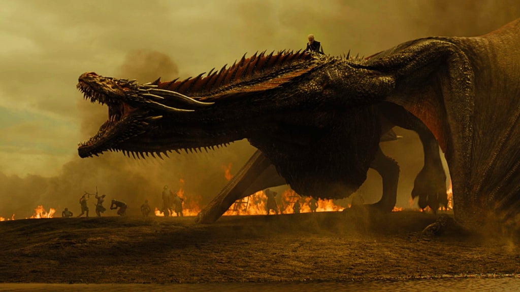 A large dragon roars on a flaming battlefield with a rider on its back in Game of Thrones