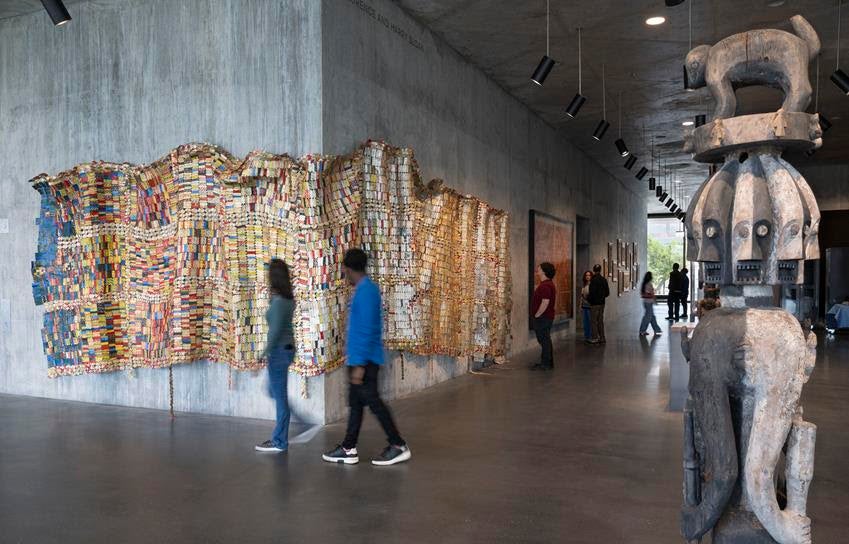 Textile Conversations: Africa and Black America installation view featuring El Anatsui's Fading Scroll, 2007, left, and an Ijo Republic of Nigeria Forest Spirit Figure, early 19th century. Source: Museum Associates/LACMA