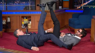 Stephen Colbert’s Interview With John Krasinski Turns Into Shots and Wrestling: ‘Can Someone Call an Ambulance Now?’ | Video
