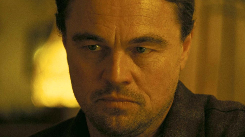 Close-up of a man with a serious, contemplative expression, softly lit in warm golden tones against a blurred background.