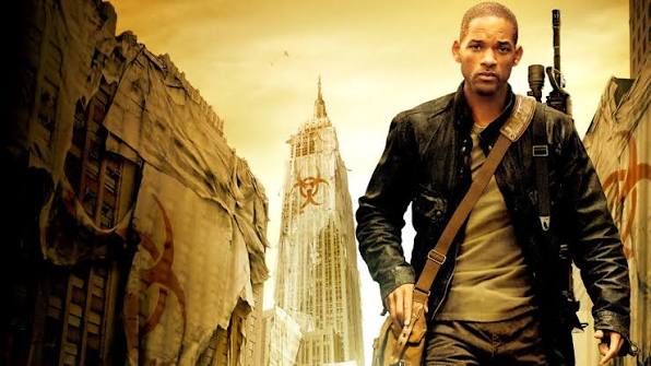 A man in a leather jacket carries a sniper rifle over his shoulder as he strides through a desolate, overgrown city street, with a skyscraper bearing a biohazard symbol looming in the sepia-toned background.