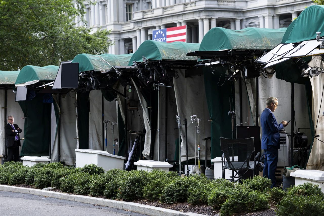 White House TV correspondents prepare to go live beside CNN’s empty broadcast position on the White House grounds.