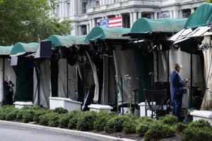 White House TV correspondents prepare to go live beside CNN’s empty broadcast position on the White House grounds.