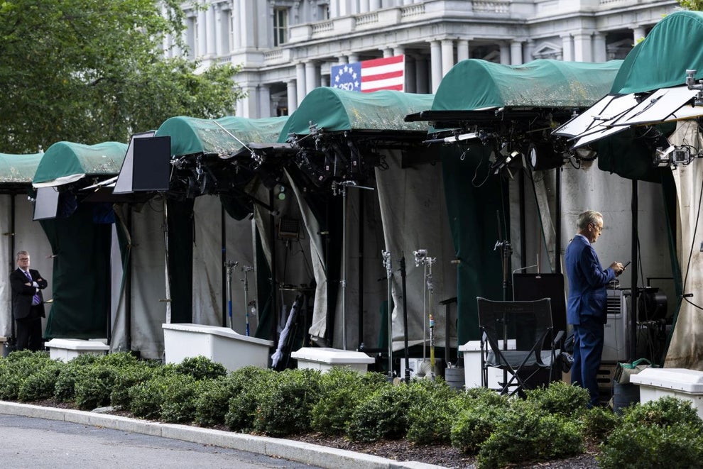 White House TV correspondents prepare to go live beside CNN’s empty broadcast position on the White House grounds.